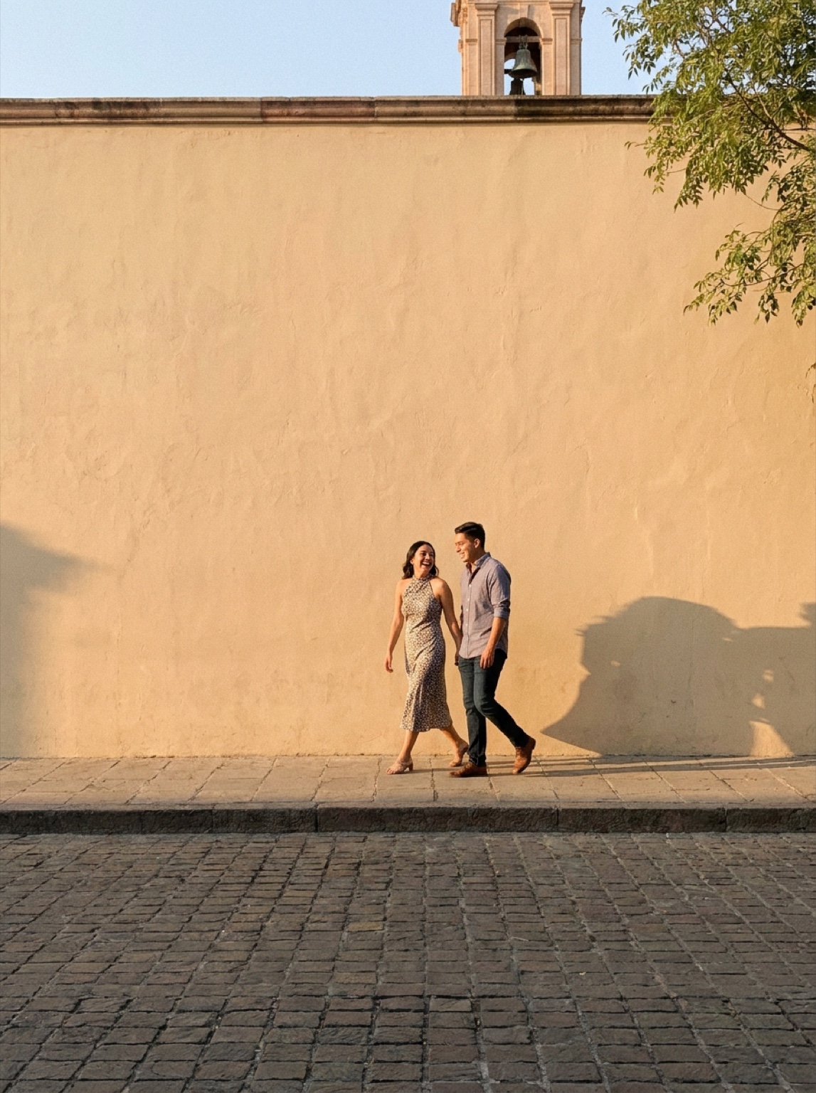 Pareja caminando junto a un muro cálido en un pueblo latinoamericano